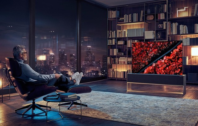 Egy frfi keresztbe tett lbakkal egy tmls szken l, egy LG SIGNATURE felcsavarhat OLED TV fel fordulva.