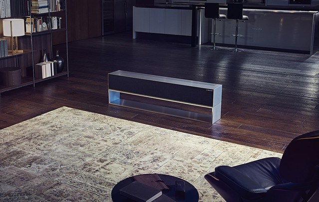 Egy frfi egy nagy ablaknak tmaszkodik, s az jszakai vrost nzi, mellette egy LG SIGNATURE felcsavarhat OLED TV vonalszer? nzet zemmdban.
